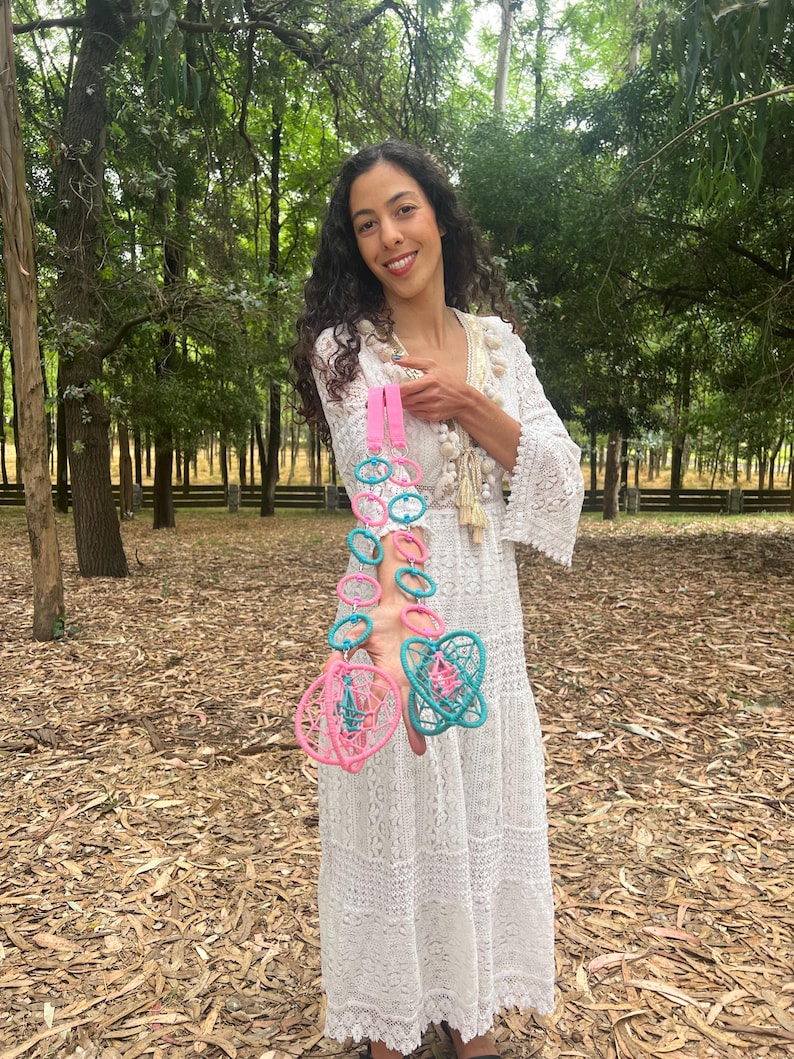 May include: Two decorative hanging ornaments featuring interconnected pink and teal plastic rings. Each ornament ends in a spherical, cage-like structure woven with matching pink and teal thread, suspended from a bright pink fabric strap.