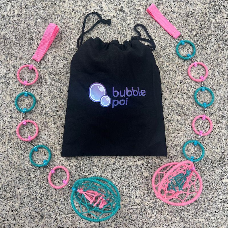 May include: A black drawstring bag with the text bubble poi and a bubble graphic, flanked by two poi sets featuring alternating pink and teal wrapped rings, pink fabric finger loops, and spherical woven cages at the ends of the chains.