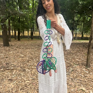 May include: A decorative hanging ornament featuring a vertical chain of alternating purple and green circular rings connected by silver metal jump rings, ending in two larger, spherical, webbed structures in matching purple and green yarn.