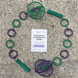May include: A bubble poi set featuring two spherical, woven net heads in green and purple, connected by a chain of alternating green and purple rings. Two green fabric finger loops are attached to the ends. A white card reads Welcome to the Bubble Poi Family.