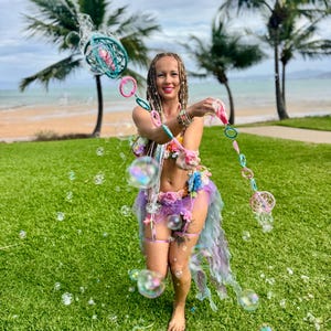 May include: A bubble wand featuring a series of interconnected circular frames in shades of teal, pink, and blue, designed for creating large bubbles. The wand is held horizontally, showcasing its colorful, lightweight structure and circular loops.