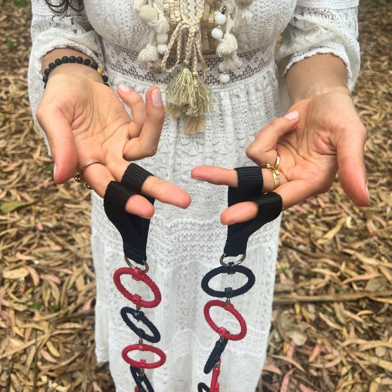 May include: A pair of exercise straps featuring black nylon webbing loops attached to a vertical chain of alternating red and dark blue circular rings. The rings are connected by small metal links, creating a long, flexible, and segmented fitness tool.