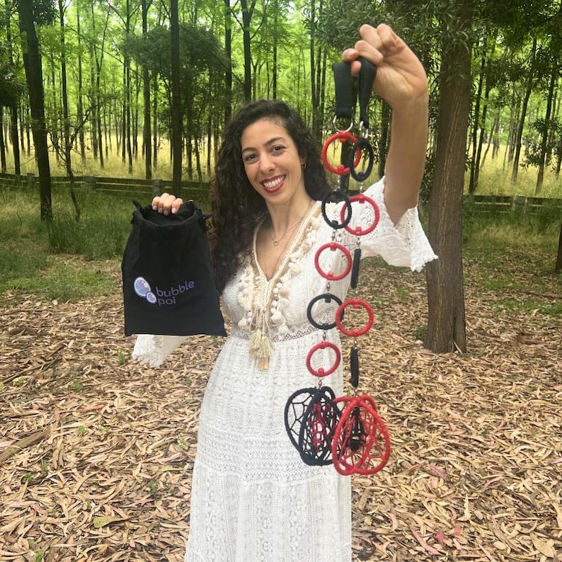 May include: A black drawstring bag with the text bubble poi printed in white, and a set of poi consisting of alternating red and black rings connected by black cords, ending in two spherical structures made of red and black woven cord loops.