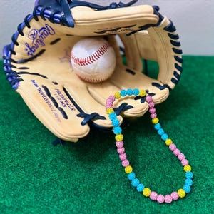 May include: A baseball glove with a baseball inside and a colorful beaded necklace with pink, yellow, and blue beads.