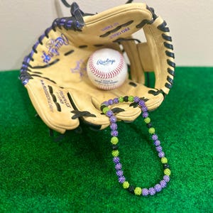 May include: A baseball glove with a baseball inside and a purple and green beaded necklace resting on top of the glove.