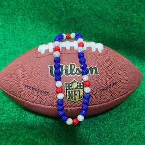 May include: A red, white, and blue beaded bracelet with a football in the background. The football is brown and has the word "Wilson" and the NFL logo on it.