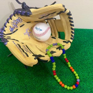 May include: A baseball glove with a purple and white trim, a baseball, and a colorful beaded necklace. The glove is labeled "PRO-MODEL" and "PRO-GLOVE".