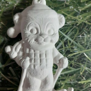 May include: White ceramic ornament of a cartoon animal wearing a hat and scarf, skiing down a hill. The ornament is blank and ready to be painted.