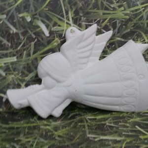 May include: White ceramic angel ornament with wings and a dress. The angel is holding a trumpet in its hand.