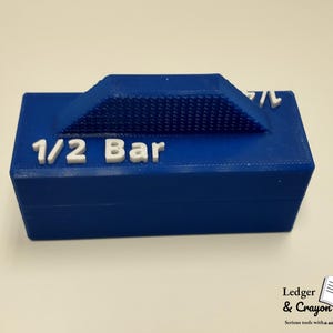 May include: A blue rectangular object with the text "1/2 Bar" in white. The top of the object has a textured, triangular section. The object is likely a tool or a component for a larger system.