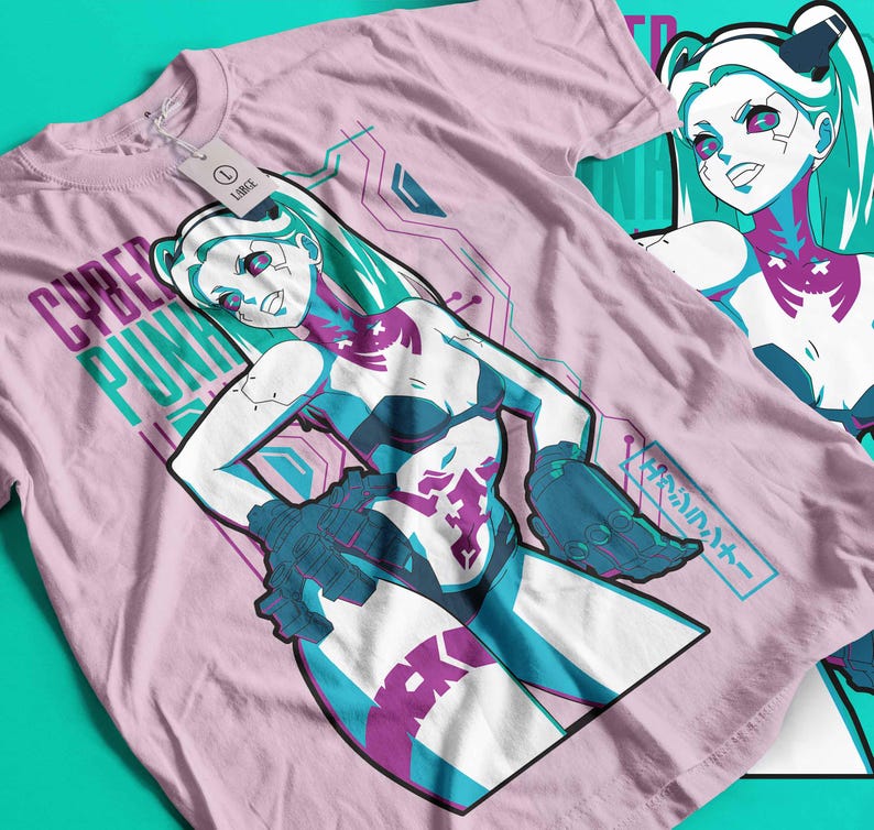 May include: Pale pink t-shirt featuring a female anime character in blue, purple, and white. The text "CYBER PUNK" is printed on the shirt. Another t-shirt with the same design is visible in the background.