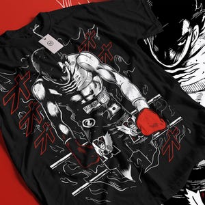 May include: Black t-shirt featuring a detailed illustration of a boxer in a fighting stance, wearing red gloves and shorts with the word "MAMORU". The design includes Japanese text and a stylized ring.