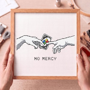 Pode incluir: Arte de ponto cruz em uma moldura de madeira. O design retrata duas mãos alcançando um cartão, com o texto "NO MERCY" abaixo. O cartão apresenta cores vermelha, amarela, verde e azul. As mãos são em tons de cinza e branco.