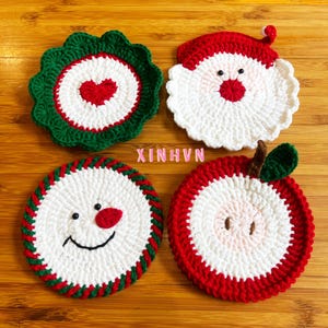 May include: Four handmade crochet coasters in festive designs. One is green with a red heart, another is a Santa face, a snowman, and an apple. The coasters are white, red, and green, perfect for holiday decor. The text "XINHVN" is visible.