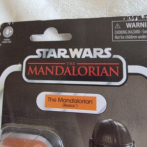 May include: A Star Wars The Mandalorian action figure package. The black package features the Star Wars logo and the words "The Mandalorian" in red and white. The figure is labeled "The Mandalorian (Beskar)".
