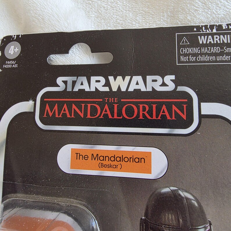 May include: A Star Wars The Mandalorian action figure package. The black package features the Star Wars logo and the words "The Mandalorian" in red and white. The figure is labeled "The Mandalorian (Beskar)".