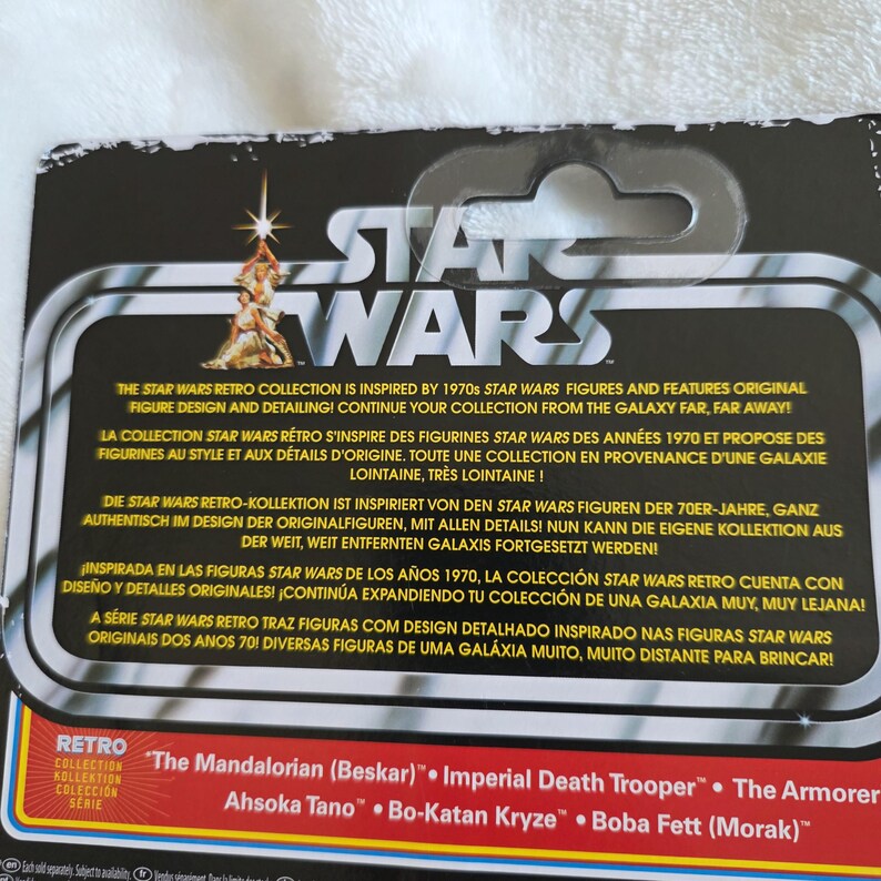 May include: Star Wars Retro Collection packaging. The black and white packaging features the Star Wars logo and text in multiple languages. The bottom of the packaging lists several character names, including "The Mandalorian (Beskar)" and "Imperial Death Trooper."
