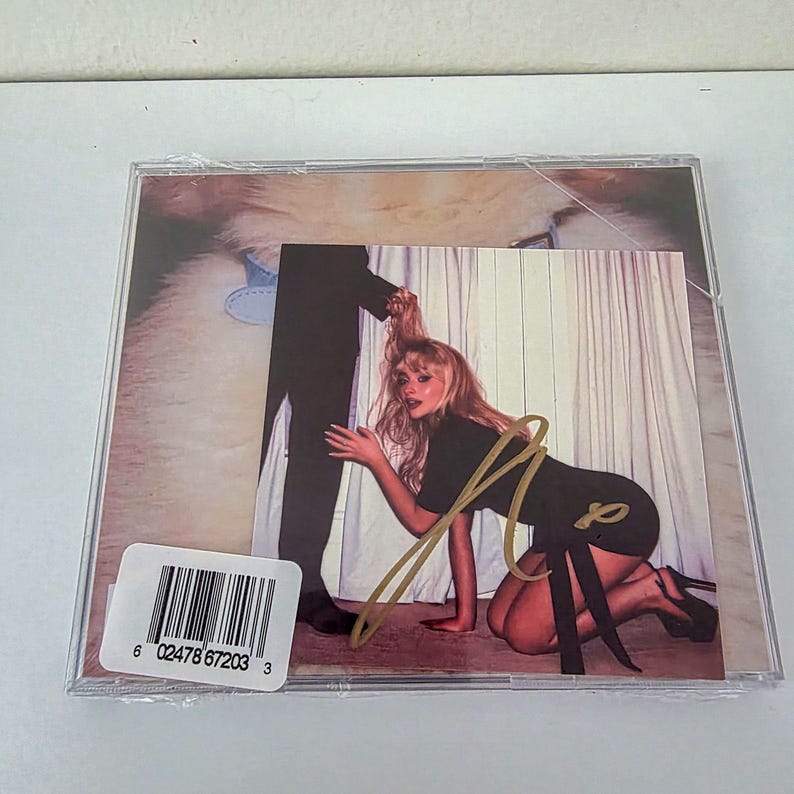 Pu&ograve; includere: Un'immagine di una custodia per CD con una copertina raffigurante una donna in ginocchio, con le gambe e il braccio di una persona sullo sfondo. La donna indossa un vestito nero e tacchi alti. La custodia del CD ha un adesivo con codice a barre e un autografo.