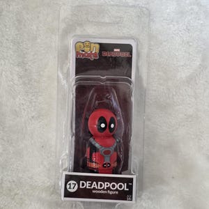 Peut inclure: Une figurine en bois Deadpool Pin Mate dans un emballage en plastique transparent. La figurine est rouge et noire avec des taches oculaires blanches. L'emballage porte le texte Pin Mate, Marvel Deadpool, le numéro 17 et Deadpool wooden figure.