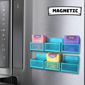 May include: A set of six turquoise magnetic tea bag organizers with a honeycomb pattern. The organizers are attached to a stainless steel refrigerator door. Each organizer holds a stack of tea bags with different flavors and names, including "Echinacea", "Take a moment just for you", "Blueberry Sage", "Keep calm sleep on", "Yogi", and "You deserve a break Enjoy it!"