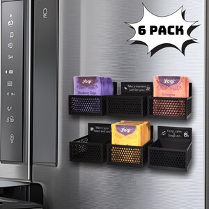 May include: Six black metal magnetic tea bag organizers with six different Yogi tea boxes. The tea boxes are purple, orange, yellow, and black with white text. The text on the boxes reads "Blueberry Sage", "Take a moment, just for you", "Echinacea", "Warm your heart and soul", "Keep calm, Steep on."