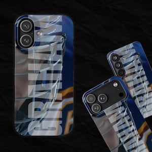 May include: A collection of phone cases with a blue and white design. The cases feature a clear overlay with the word "GAME" in a bold, stylized font. The cases have a black camera module and a blue border.