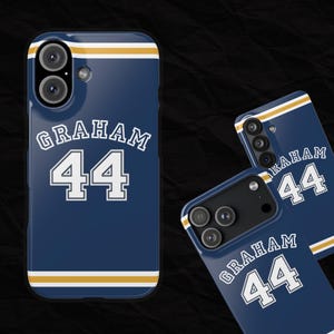 May include: Navy blue phone case with the name "GRAHAM" and the number "44" in white block letters. The case has a gold stripe at the top and bottom. The phone case is shown from multiple angles.