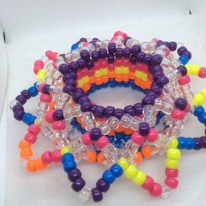 Op de afbeelding: Een kleurrijke kandi armband gemaakt van plastic kralen in paars, roze, oranje, geel, blauw en transparant. De armband heeft de vorm van een bloem met meerdere lagen kralen.