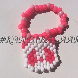 Puede incluir: Pulsera kandi rosa y blanca con un encanto cuadrado. El encanto est&aacute; hecho de cuentas rosas y blancas y tiene un patr&oacute;n de cuadros. La pulsera tiene el hashtag #KANDIBAZAAR.