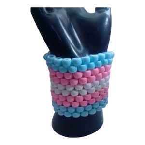 Puede incluir: Un brazalete de cuentas azul, rosa y blanco con un diseño que se asemeja a la bandera del orgullo transgénero.