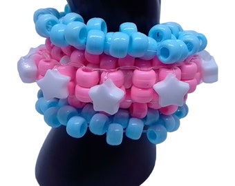 Puede incluir: Un brazalete kandi de varias capas con cuentas rosas y azules y abalorios de estrellas blancas.