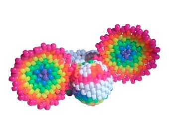 Puede incluir: Tres adornos de cuentas de colores arcoíris, dos son planos y circulares, y uno es una esfera. Las cuentas están dispuestas en un patrón circular con un centro blanco.