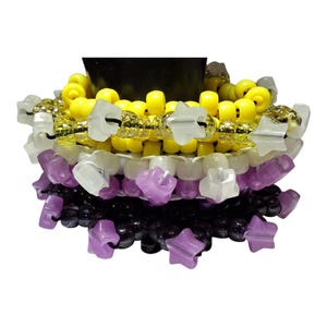 May include: A stack of three beaded bracelets featuring yellow, white, and purple plastic beads. The bracelets include translucent star-shaped beads interspersed with round beads, all strung on elastic cord for a flexible fit.