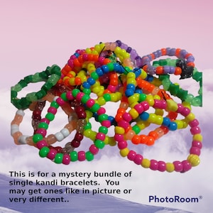 Op de afbeelding: Een stapel kleurrijke kandi-armbanden gemaakt van plastic kralen. De armbanden zijn in verschillende kleuren, waaronder groen, roze, geel, oranje, blauw en paars.