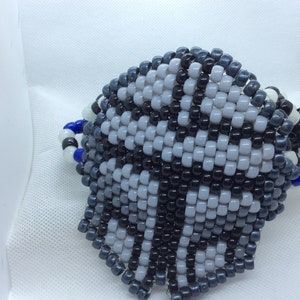 Op de afbeelding: Een armband van zwarte, witte en grijze kralen met een geometrisch patroon. De armband is gemaakt van kleine, ronde kralen en is met een blauw touwtje aan elkaar gebonden.