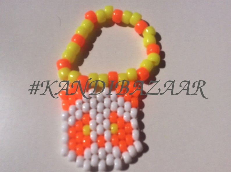 Puede incluir: Un brazalete de cuentas amarillas y naranjas con un dije de cuentas blancas y naranjas que dice "#KANDIBAZAAR".