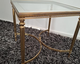 May include: A rectangular side table with a clear glass top and a gold-colored metal frame. The table has four legs and decorative detailing around the top edge. The table is approximately 24 inches long, 16 inches wide, and 20 inches tall.