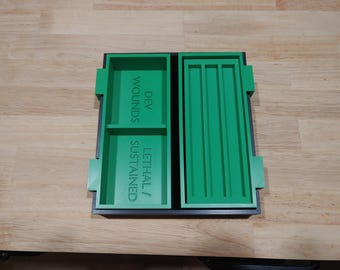 May include: A green plastic organizer with two compartments. The left compartment has the text "DEV WOUNDS / LETHAL / SUSTAINED". The right compartment has five slots.
