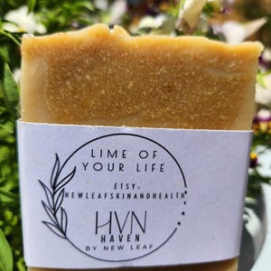 May include: A rectangular bar of handmade soap with a light brown color and a textured surface. A white label wrapped around the soap features the text "LIME OF YOUR LIFE" and "HVN HAVEN BY NEW LEAF".