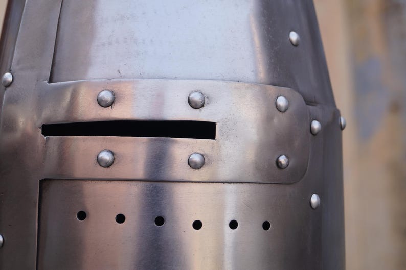 Peut inclure: Gros plan sur un casque de chevalier m&eacute;di&eacute;val en acier poli. Le casque comporte une fente oculaire rectangulaire et est rivet&eacute;. Le m&eacute;tal a une surface r&eacute;fl&eacute;chissante, et le design est simple et fonctionnel.