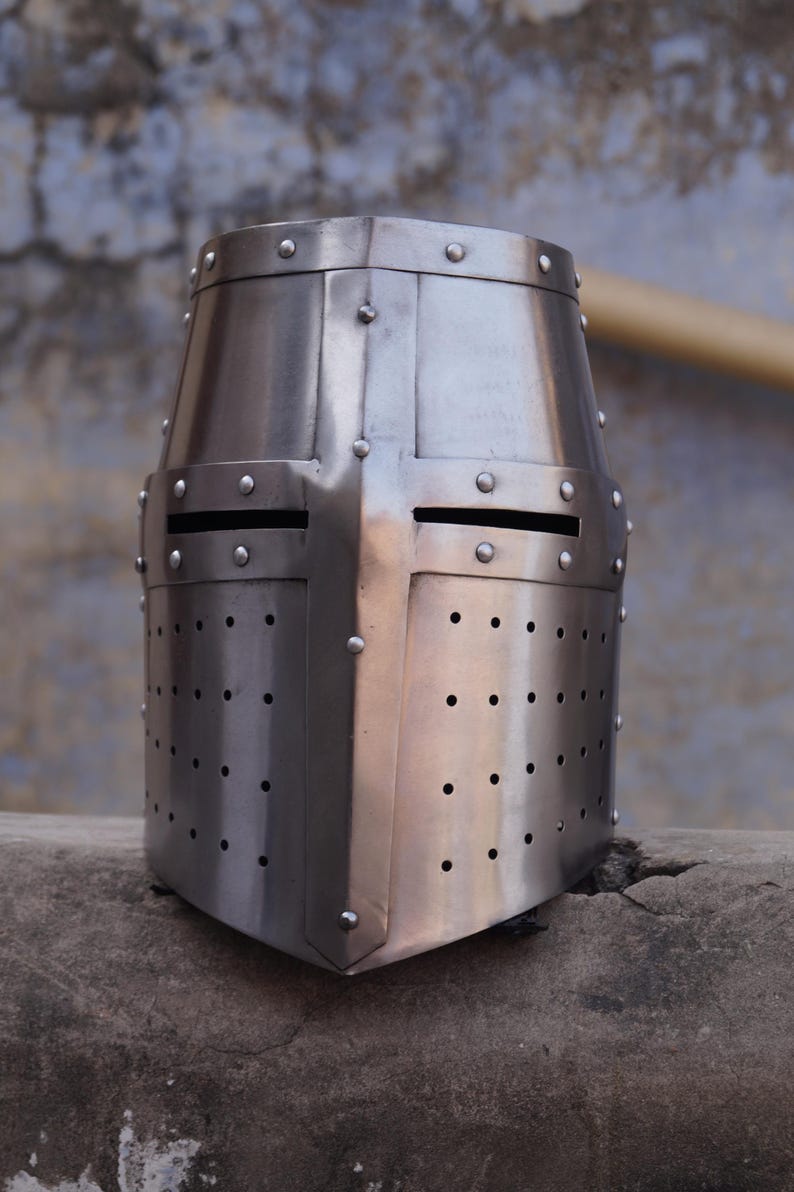 Peut inclure: Casque de crois&eacute; m&eacute;di&eacute;val argent&eacute; et poli. Le casque pr&eacute;sente un dessus plat, un motif en forme de croix et de petits rivets. Il comporte des fentes pour les yeux et de nombreux trous de ventilation.