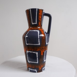 May include: A blue and orange ceramic vase with a geometric pattern. The vase has a handle and a wide mouth.