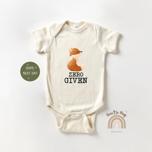 May include: A cream-colored baby onesie with a brown fox illustration and the text "Zero Given".