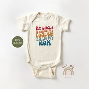 May include: A cream-colored baby onesie with the text "My Uncle is definitely cooler than my Mom" in a rainbow color scheme.