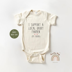 May include: A cream-colored baby onesie with the text "I support a local dairy farmer (my mama)" in black. Two small pink hearts are above the text.