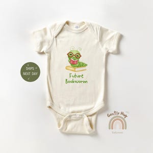 May include: A white baby onesie with a green worm wearing glasses and reading a book. The text "Future Bookworm" is printed below the worm.