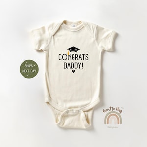 May include: A white baby onesie with a black graduation cap and the text "Congrats Daddy!" in black. A small black heart is below the text.