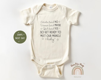 May include: A beige baby onesie with the text "Nature Said NO, Science Said MAYBE, God Said YES, SO GET READY TO MEET OUR MIRACLE baby" printed in black.