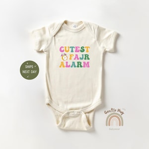 May include: A white baby onesie with the text "CUTEST FAJR ALARM" in colorful retro font. The text includes a small alarm clock graphic.