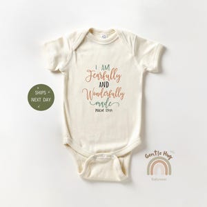 May include: Cream-colored baby bodysuit with short sleeves. The text "I AM Fearfully and Wonderfully made PSALM 139:14" is printed on the front in shades of brown, green, and teal. The bodysuit has a snap closure.